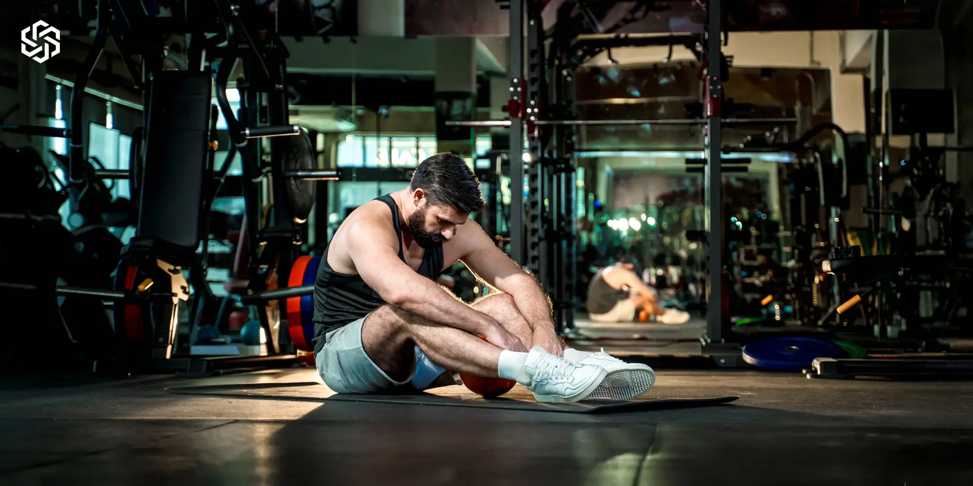 Tired man sitting on a gym floor, representing fatigue and low energy caused by hormone imbalance