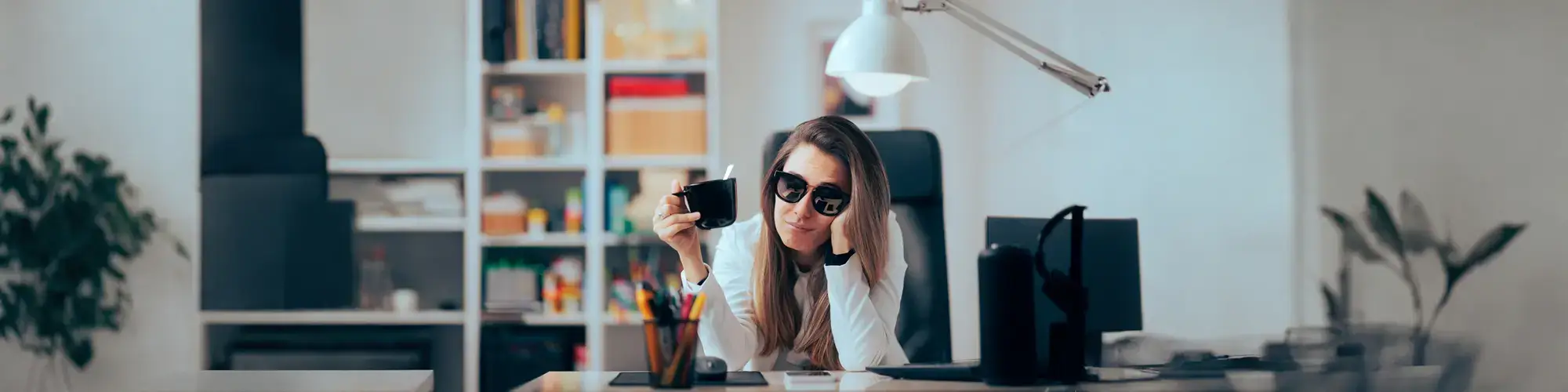 Woman with hangover symptoms at desk drinking coffee, representing need for Hangover IV Recovery therapy in Lake Forest IL