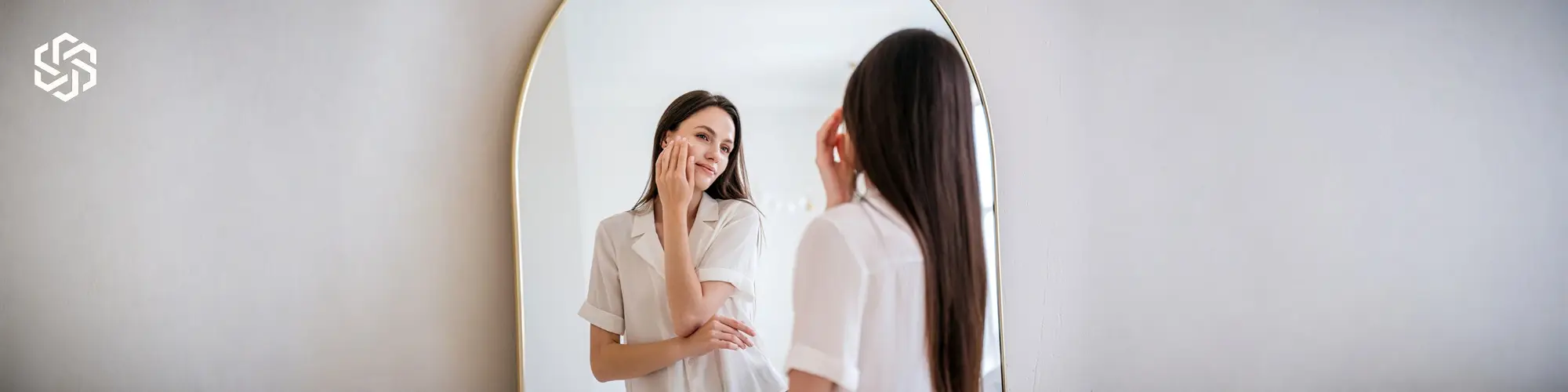 Woman looking in a mirror with healthy glowing skin and long hair representing beauty and wellness benefits of Biotin Vitamin B7 injections.