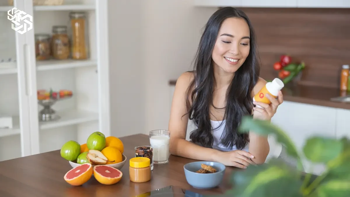 Woman holding a supplement bottle at a kitchen table with fruit