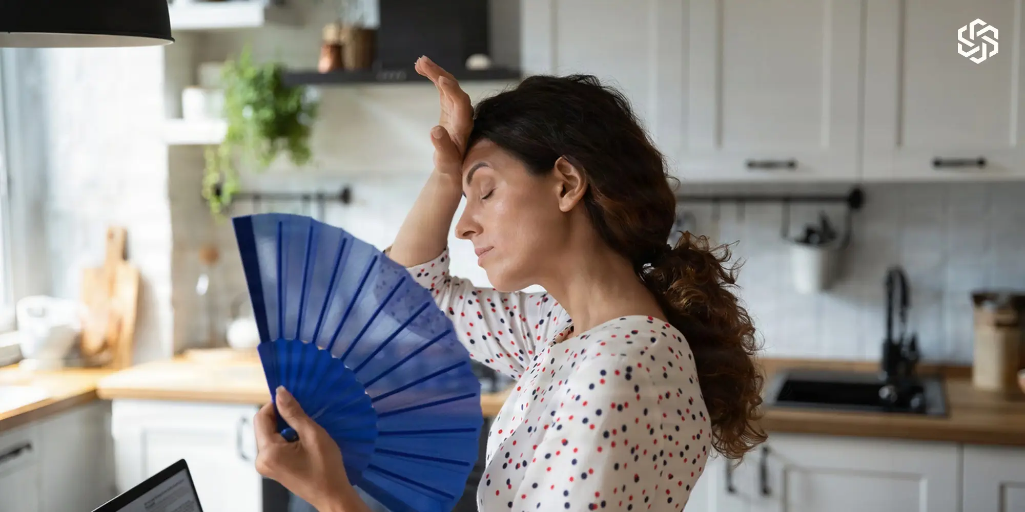 Woman fanning herself in her kitchen during a hot flash