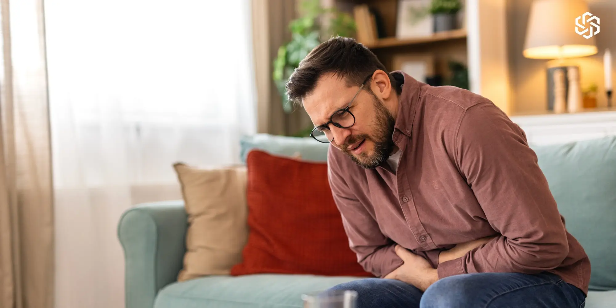 Man sitting on a couch holding his stomach in discomfort
