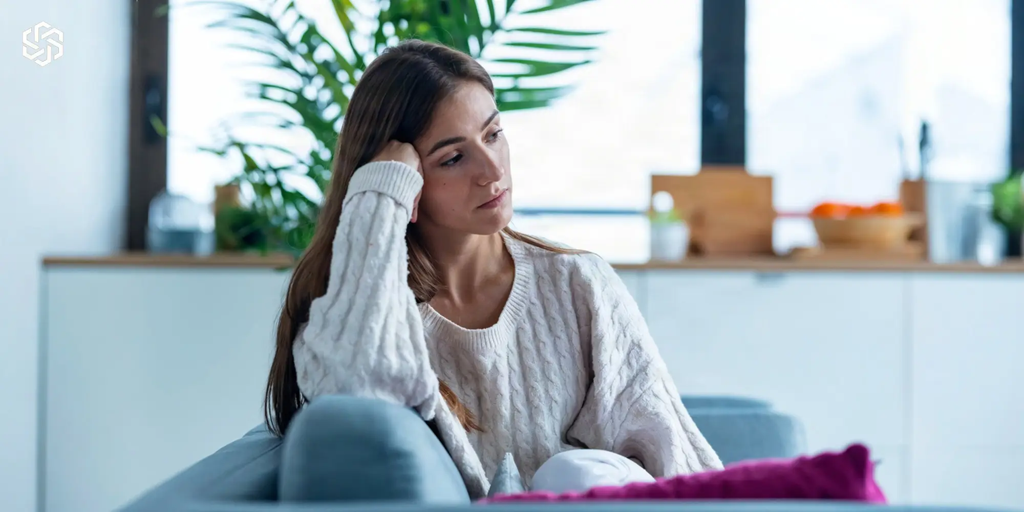 Woman sitting on a couch looking thoughtful with her hand to her head