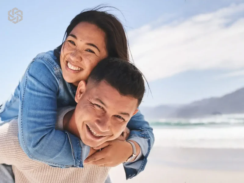Smiling couple on the beach, woman riding piggyback