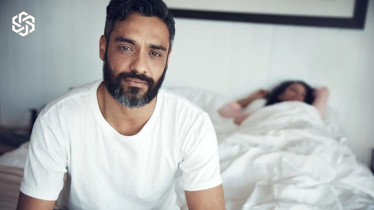 Man sitting on the bed while his partner sleeps