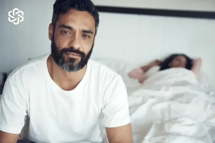 Man sitting on the bed while his partner sleeps