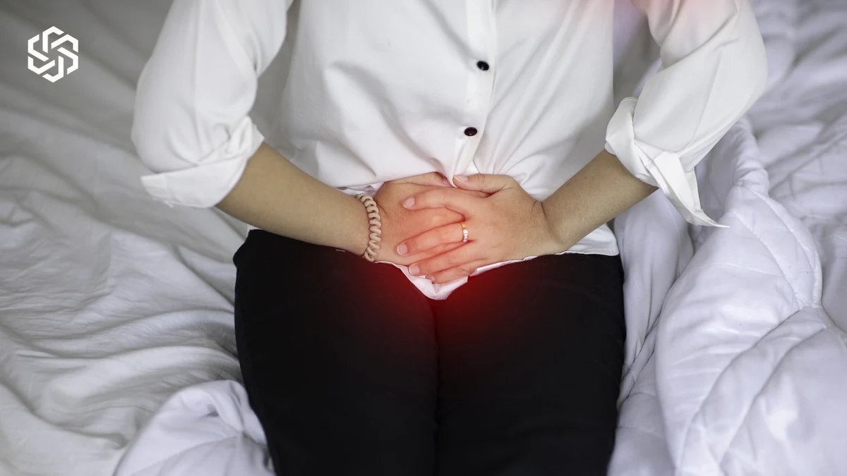 Woman sitting on a bed holding her lower abdomen