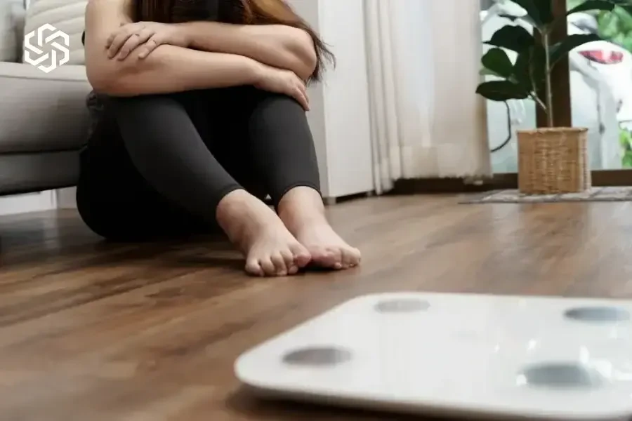 Discouraged woman sitting near a bathroom scale