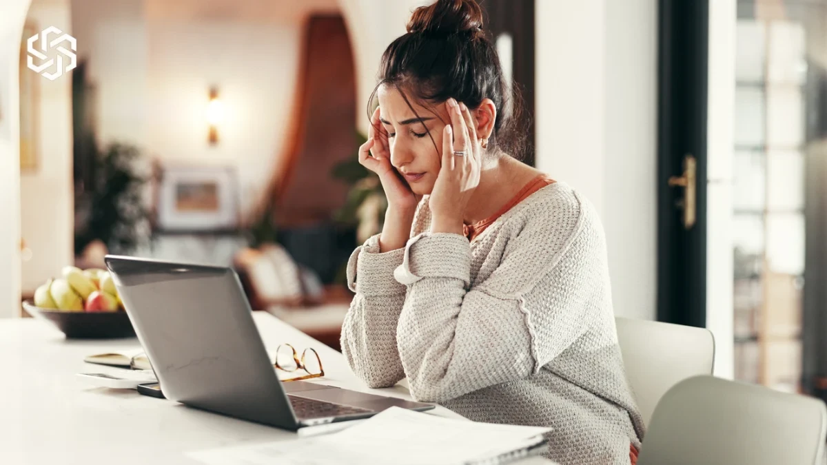 Woman with a headache working at her laptop, struggling with brain fog