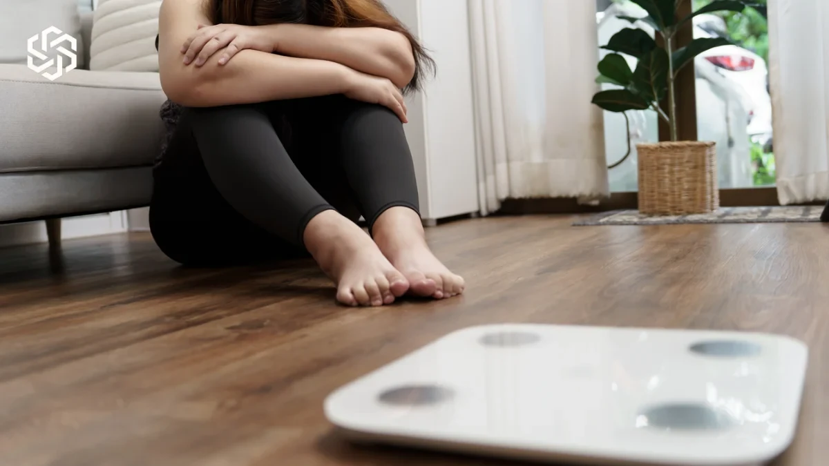 Discouraged woman sitting near a bathroom scale after not losing weight
