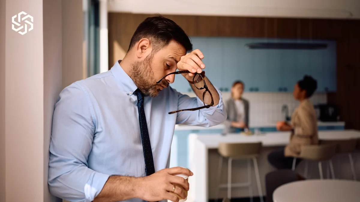 Stressed man rubbing his eyes at work