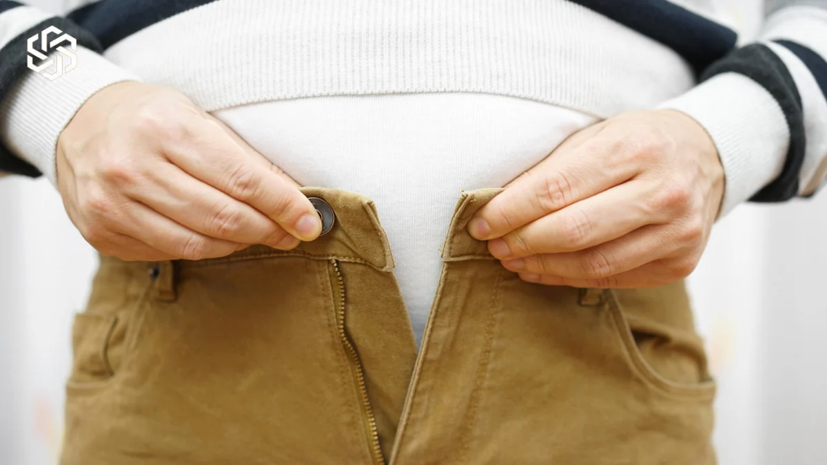 Man struggling to button his pants