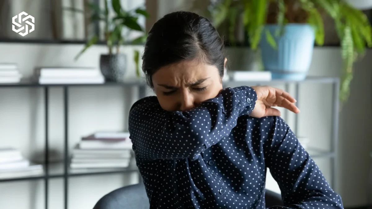 Woman coughing into her elbow at work, a common trigger for stress incontinence leaks