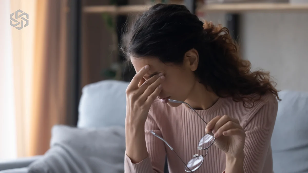 Woman with a headache removing her glasses, illustrating hormone symptoms with normal labs